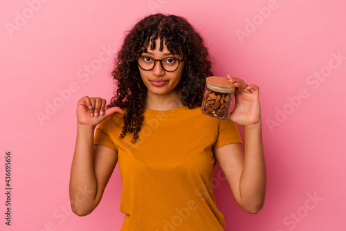 Young mixed race woman holding an almond jar isolated on pink background showing a dislike gesture, thumbs down. Disagreement concept.