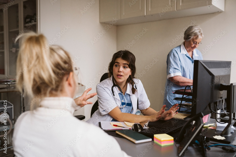 Female medical expert talking with disabled woman while senior nurse working at desk Female medical expert talking with disabled woman while senior nurse working at desk