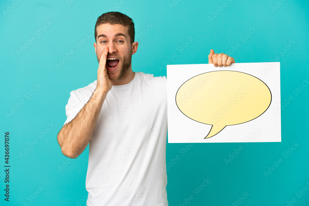 Handsome blonde man over isolated blue background holding a placard with speech bubble icon and shouting Handsome blonde man over isolated blue background holding a placard with speech bubble icon and shouting
