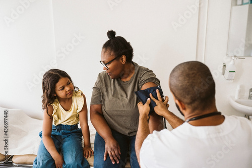 Mother talking with daughter while male doctor measuring blood pressure photo