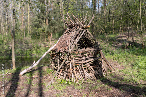 Handmade hut made of branches in the forest near pond on sunset.