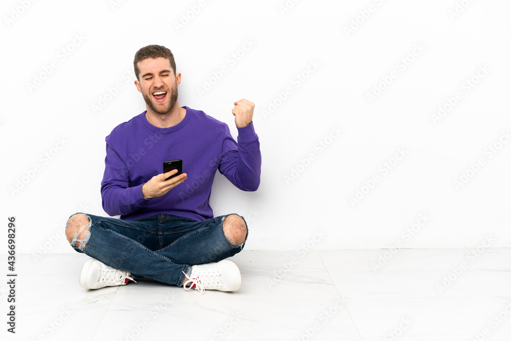 Young man sitting on the floor with phone in victory position