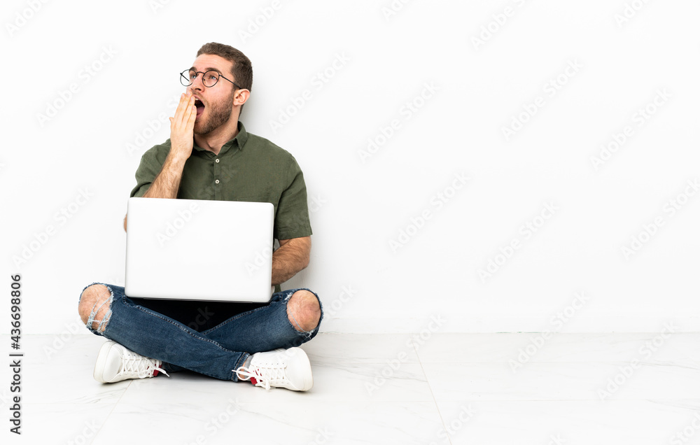 Young man sitting on the floor yawning and covering wide open mouth with hand Young man sitting on the floor yawning and covering wide open mouth with hand