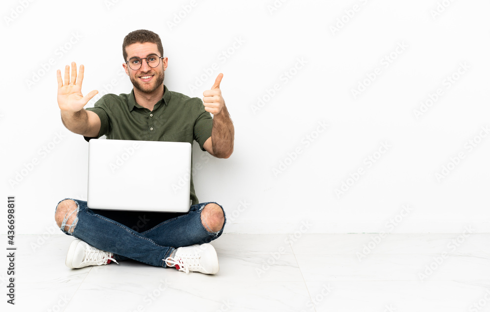 Young man sitting on the floor counting six with fingers Young man sitting on the floor counting six with fingers