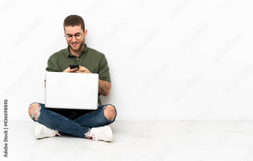 Young man sitting on the floor sending a message with the mobile Young man sitting on the floor sending a message with the mobile