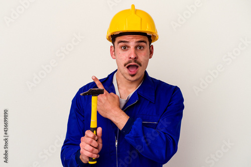 Young caucasian worker man holding a hammer isolated on white background pointing to the side