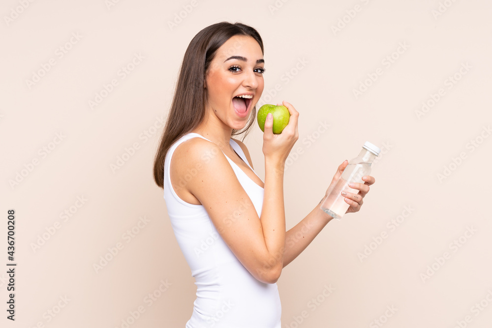 Young caucasian woman isolated on beige background with an apple and with a bottle of water Young caucasian woman isolated on beige background with an apple and with a bottle of water