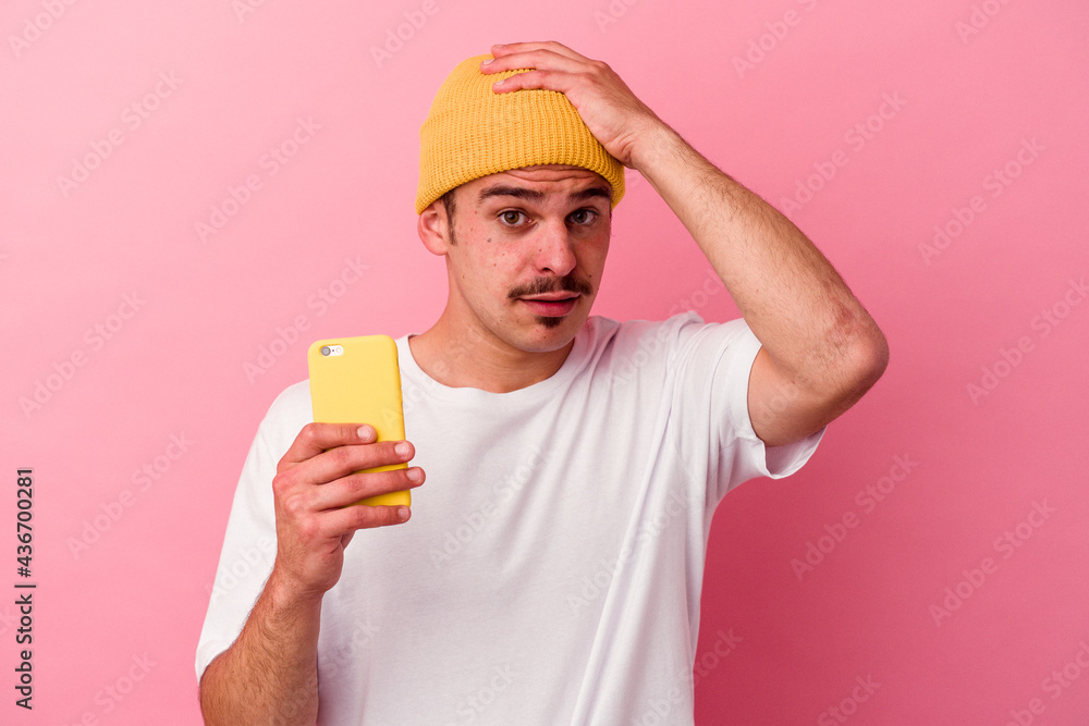 Young caucasian man holding a mobile phone isolated on pink background being shocked, she has remembered important meeting.