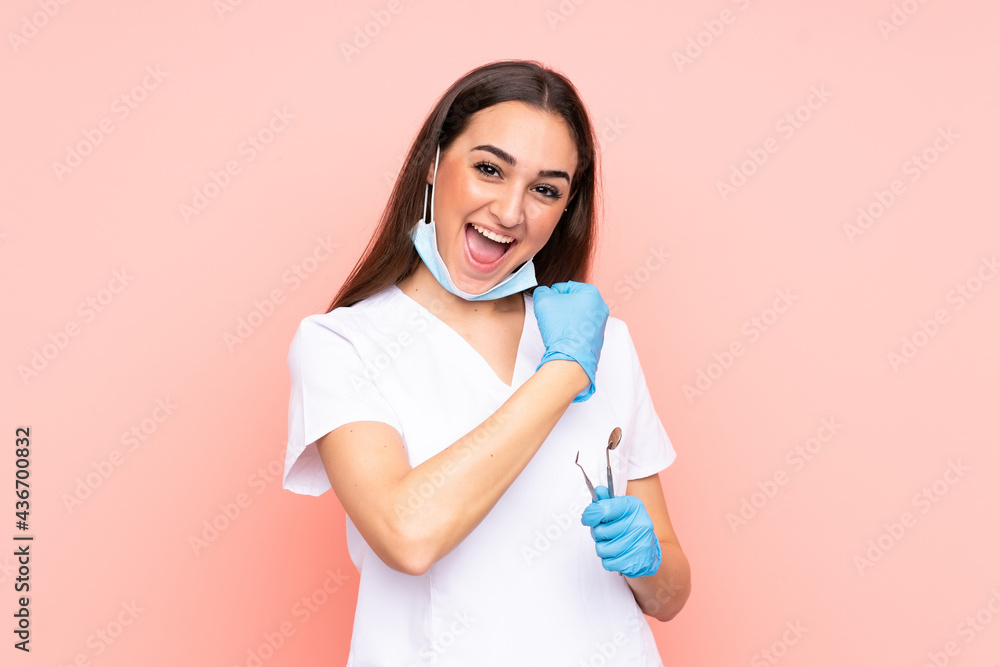 Woman dentist holding tools isolated on pink background celebrating a victory Woman dentist holding tools isolated on pink background celebrating a victory