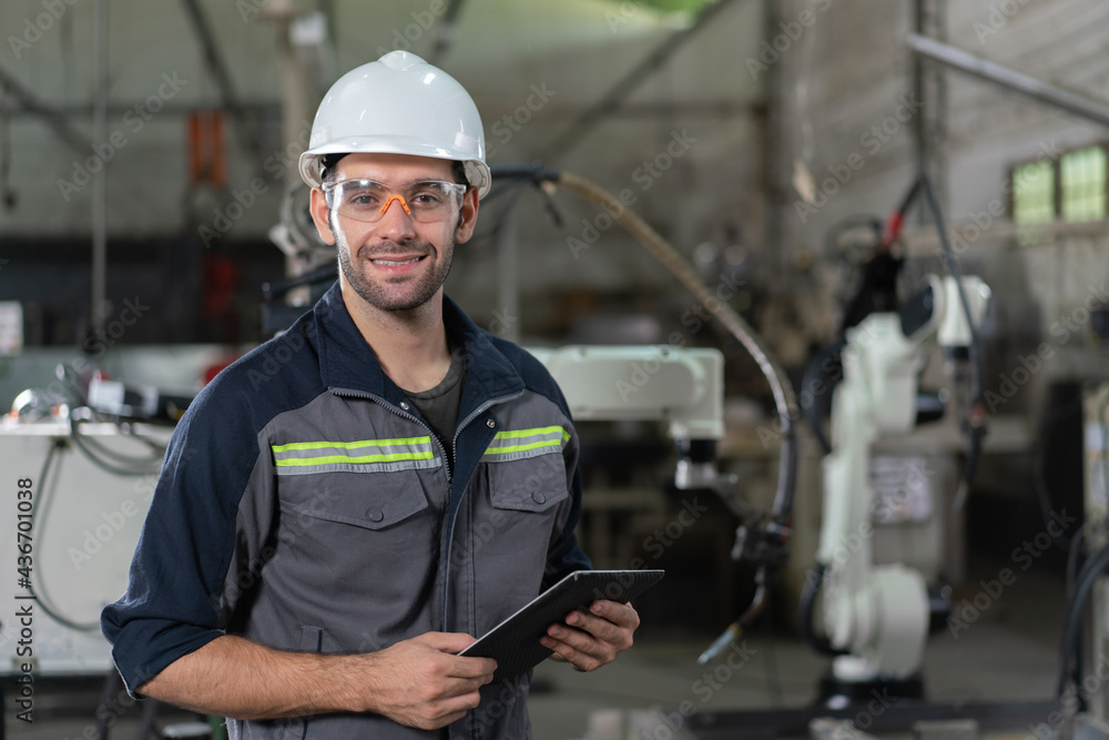 Portrait of male automation engineer smiling hold tablet for .inspection robot arm welding machine in industrial factory Portrait of male automation engineer smiling hold tablet for .inspection robot arm welding machine in industrial factory