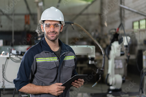 Portrait of male automation engineer smiling hold tablet for .inspection robot arm welding machine  in industrial factory © Supachai