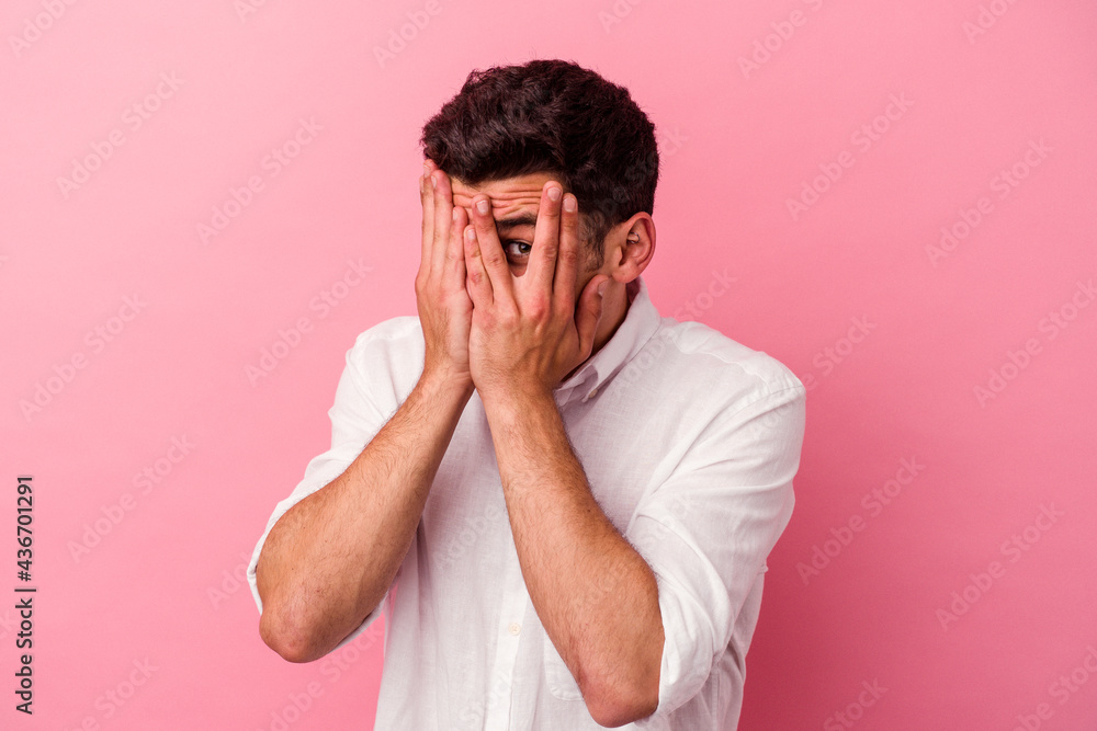 Young caucasian man isolated on pink background blink through fingers frightened and nervous. Young caucasian man isolated on pink background blink through fingers frightened and nervous.