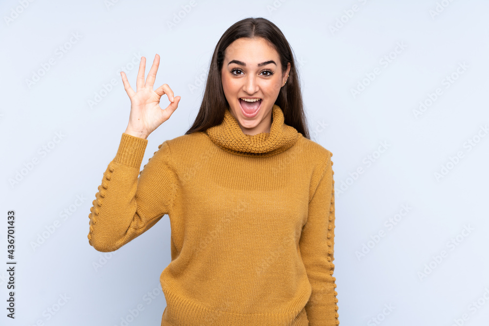 Young caucasian woman isolated on blue background surprised and showing ok sign Young caucasian woman isolated on blue background surprised and showing ok sign