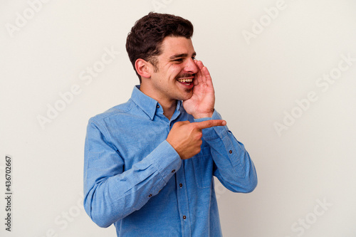 Young caucasian man isolated on white background saying a gossip, pointing to side reporting something.