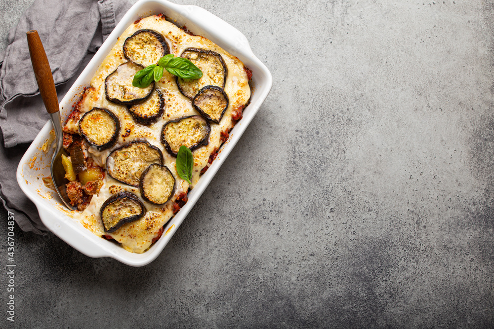 Greek mediterranean dish Moussaka with baked eggplants, ground beef in white ceramic casserole on rustic stone background from above, traditional dish of Greece, space for text