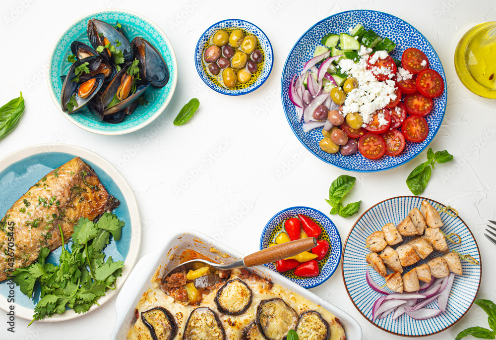 Assorted Greek dishes on white stone background from above, moussaka, grilled fish, souvlaki, greek salad, steamed mussels with herbs, appetizers of Greece from above, space for text Assorted Greek dishes on white stone background from above, moussaka, grilled fish, souvlaki, greek salad, steamed mussels with herbs, appetizers of Greece from above, space for text