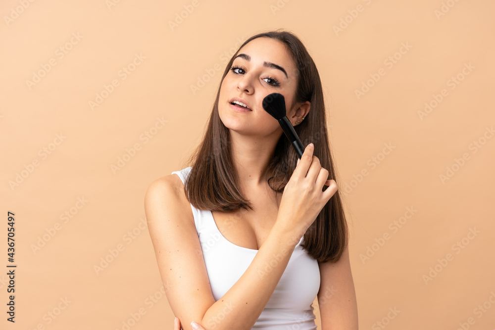 Fototapeta premium Young caucasian woman isolated on beige background holding makeup brush