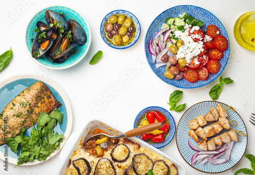 Assorted Greek dishes on white stone background from above, moussaka, grilled fish, souvlaki, greek salad, steamed mussels with herbs, appetizers of Greece from above, space for text