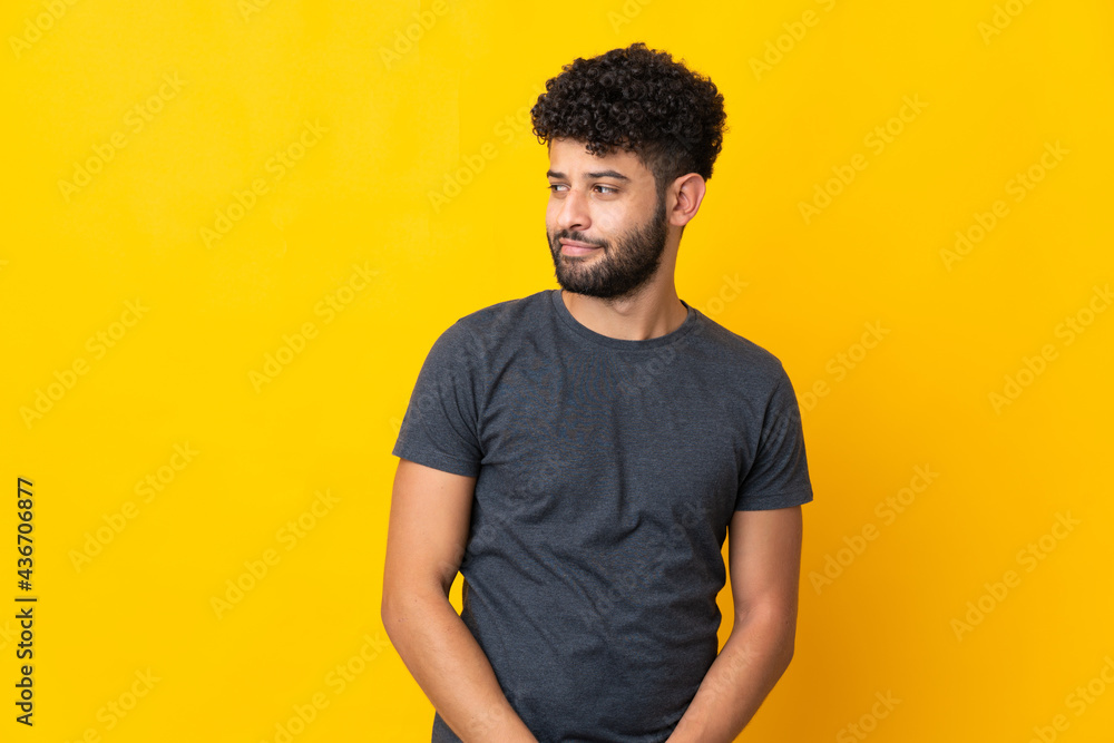 Young Moroccan man isolated on yellow background having doubts while looking side Young Moroccan man isolated on yellow background having doubts while looking side