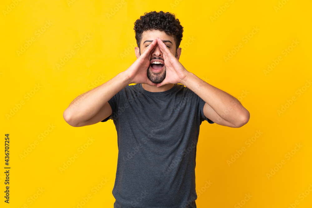 Young Moroccan man isolated on yellow background shouting and announcing something Young Moroccan man isolated on yellow background shouting and announcing something