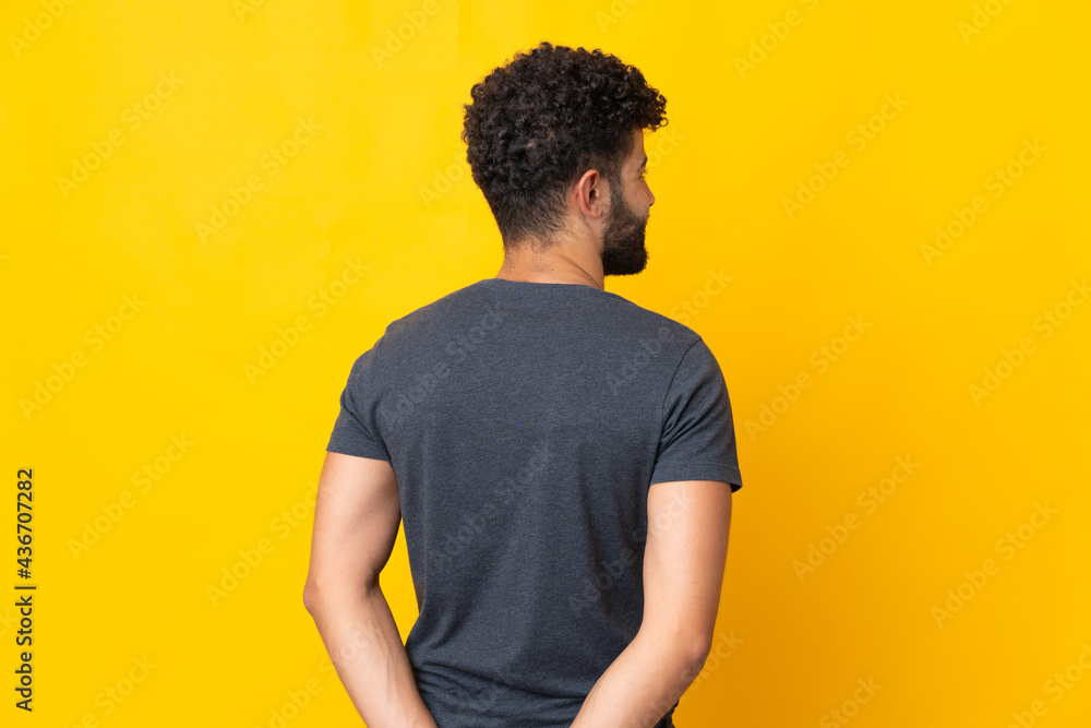 Young Moroccan man isolated on yellow background in back position and looking back Young Moroccan man isolated on yellow background in back position and looking back