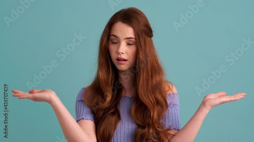 A beautiful woman is comparing something and choose on of two objects in her hand-palms standing isolated over blue wall in the studio photo