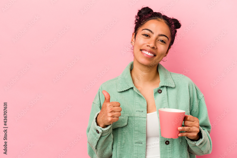 Young latin woman holding a mug isolated on pink background smiling and raising thumb up Young latin woman holding a mug isolated on pink background smiling and raising thumb up