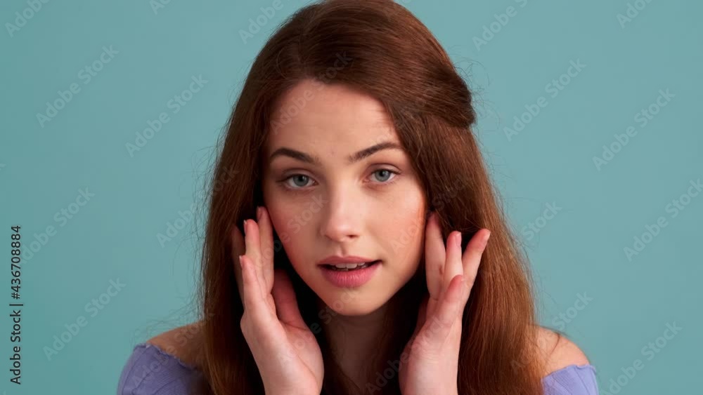 A pleased woman is looking at her face standing isolated over blue wall in the studio A pleased woman is looking at her face standing isolated over blue wall in the studio