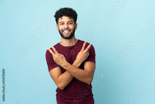 Young Moroccan man isolated on blue background smiling and showing victory sign