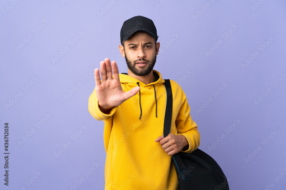Young sport Moroccan man with sport bag isolated on purple background making stop gesture