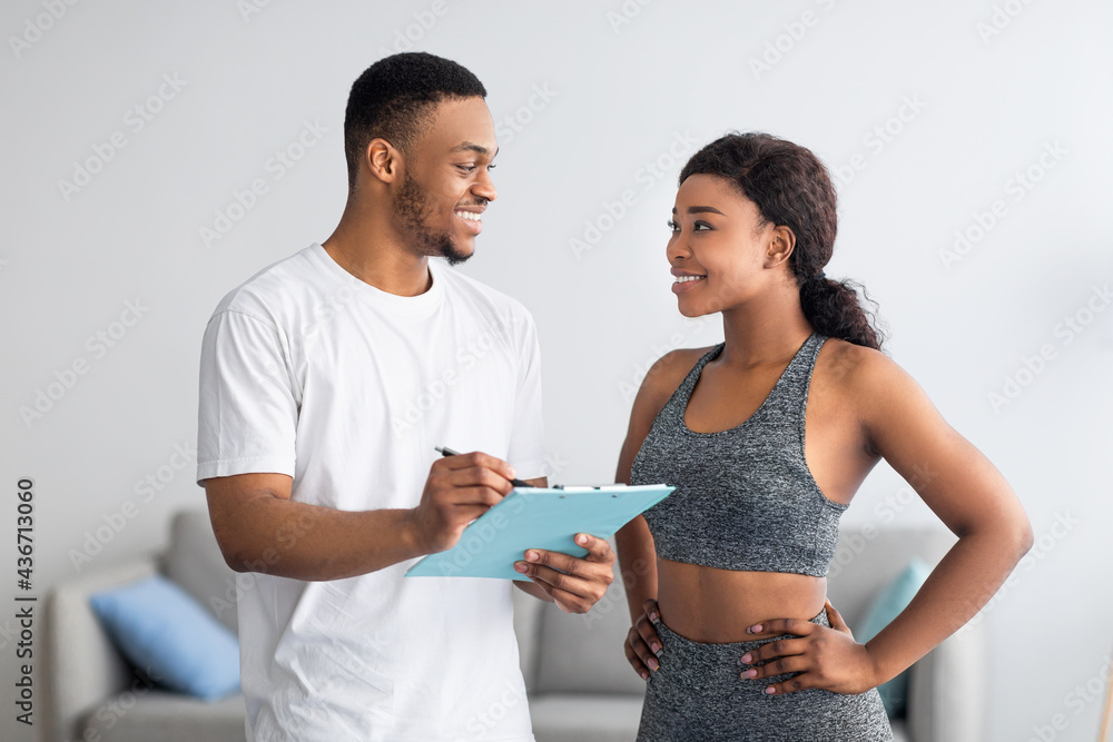 Fototapeta premium Young black couple discussing workout plan, standing together at home gym