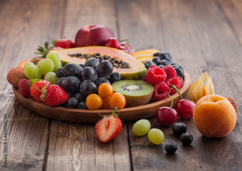 Fresh raw organic summer berries and exotic fruits in round wooden plate on light wooden kitchen background. Papaya, grapes, nectarine, orange, raspberry, kiwi, strawberry, lychees, cherry. Fresh raw organic summer berries and exotic fruits in round wooden plate on light wooden kitchen background. Papaya, grapes, nectarine, orange, raspberry, kiwi, strawberry, lychees, cherry.
