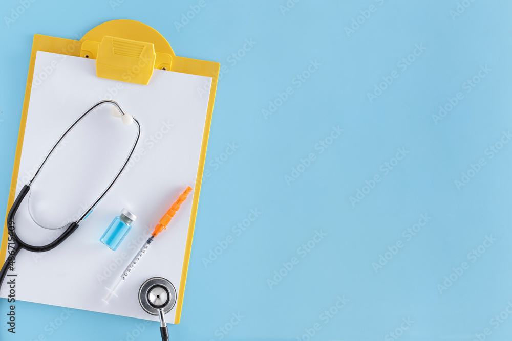 Medicine syringe with vaccine vial, stethoscope and a notepad on a blue background. Medicine syringe with vaccine vial, stethoscope and a notepad on a blue background.