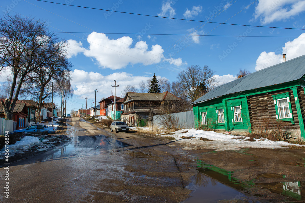 Scenic view of street in a small provincial town or village with traditional Russian wooden houses under blue sky. Spring rural landscape. Nerekhta, Kostroma region, Russia Scenic view of street in a small provincial town or village with traditional Russian wooden houses under blue sky. Spring rural landscape. Nerekhta, Kostroma region, Russia