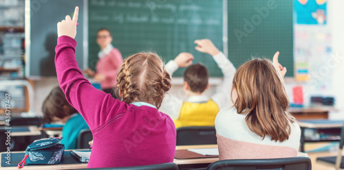 Foto Two girl students raising hands to answer a question in school class