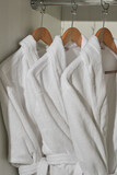 White hotel robes on a hangers in a white wardrobe.