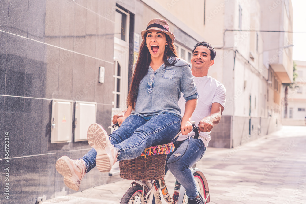 People, leisure and lifestyle concept happy young couple riding bicycle in the city - overjoyed young woman enjoy love and friendship with black boyfriend having fun
