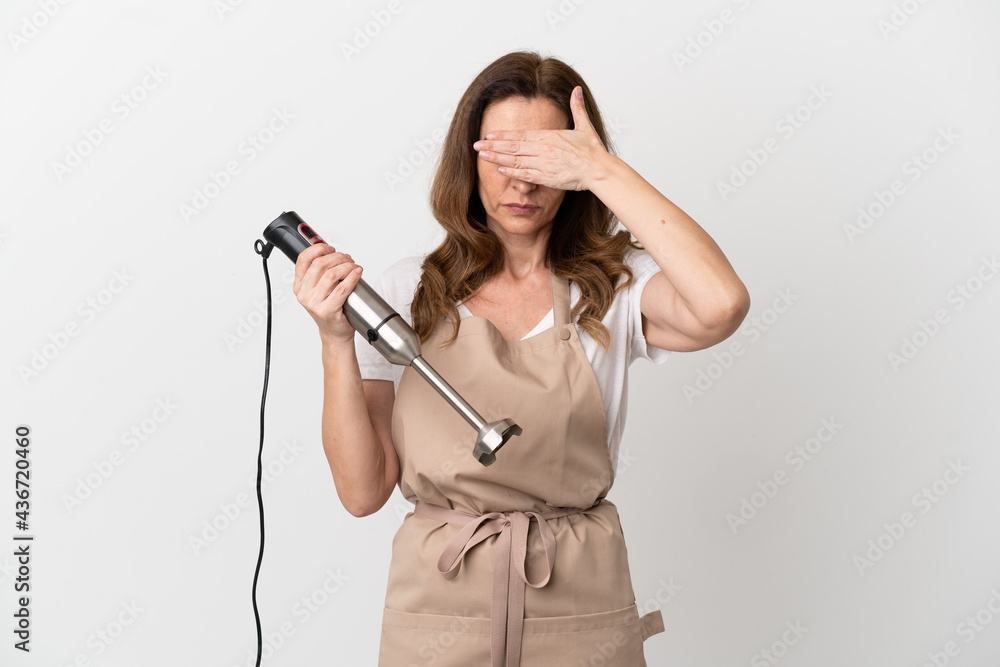 Middle aged caucasian woman using hand blender isolated on white background covering eyes by hands. Do not want to see something Middle aged caucasian woman using hand blender isolated on white background covering eyes by hands. Do not want to see something