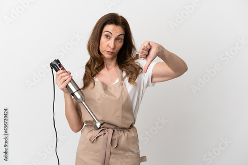 Middle aged caucasian woman using hand blender isolated on white background showing thumb down with negative expression