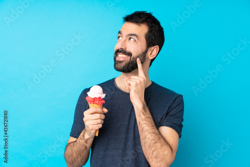 Young man with a cornet ice cream over isolated blue background thinking an idea while looking up