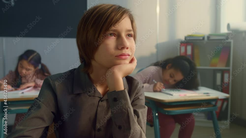 Boy studying in classroom with classmates. Male student boring during lesson Boy studying in classroom with classmates. Male student boring during lesson
