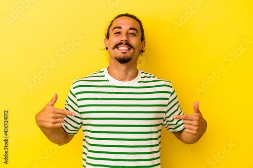 Young caucasian man with long hair isolated on yellow background points down with fingers, positive feeling.