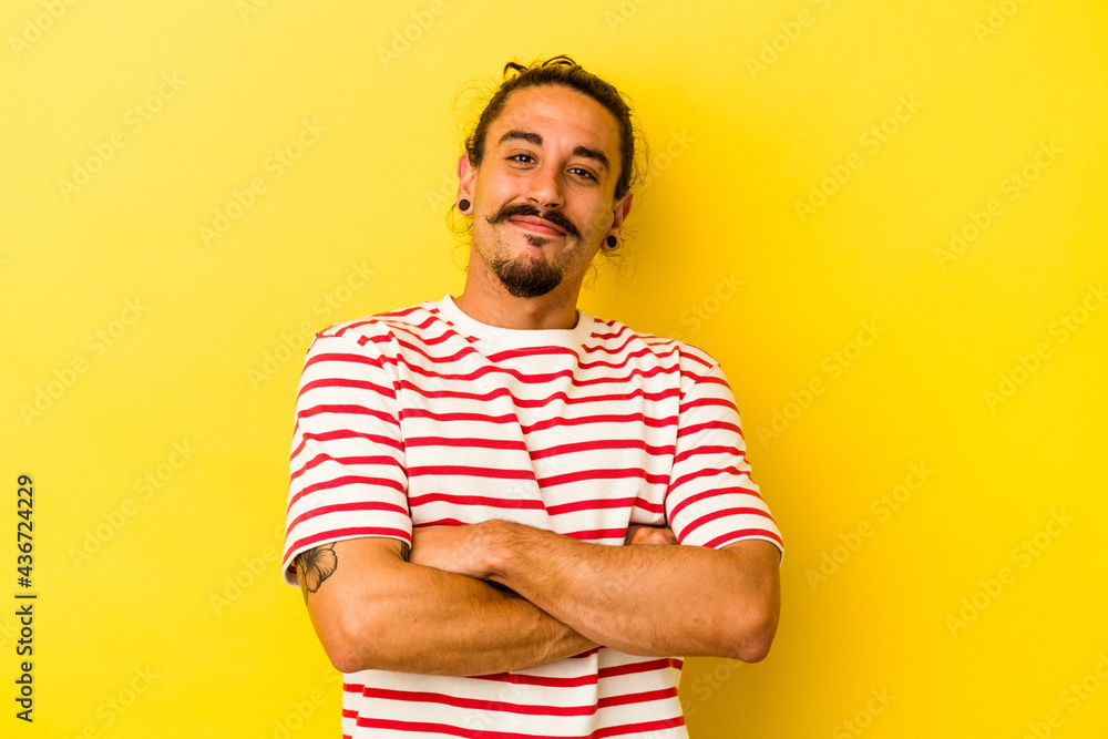 Young caucasian man with long hair isolated on yellow background who feels confident, crossing arms with determination. Young caucasian man with long hair isolated on yellow background who feels confident, crossing arms with determination.