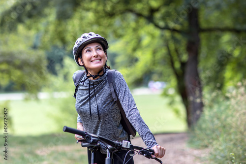 Young and happy woman in a tracksuit on a mountain bike enjoys in day ride through the park © pucko_ns