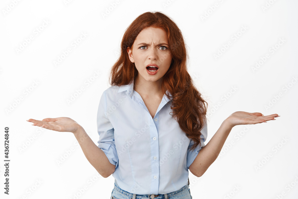 Annoyed and confused redhead business woman shrugging, staring frustrated at camera, cant understand wtf going on, standing clueless against white background Annoyed and confused redhead business woman shrugging, staring frustrated at camera, cant understand wtf going on, standing clueless against white background