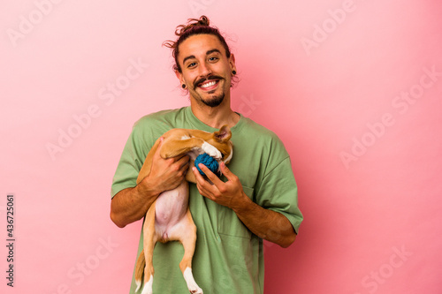 Young caucasian man holding his puppy isolated on pink background