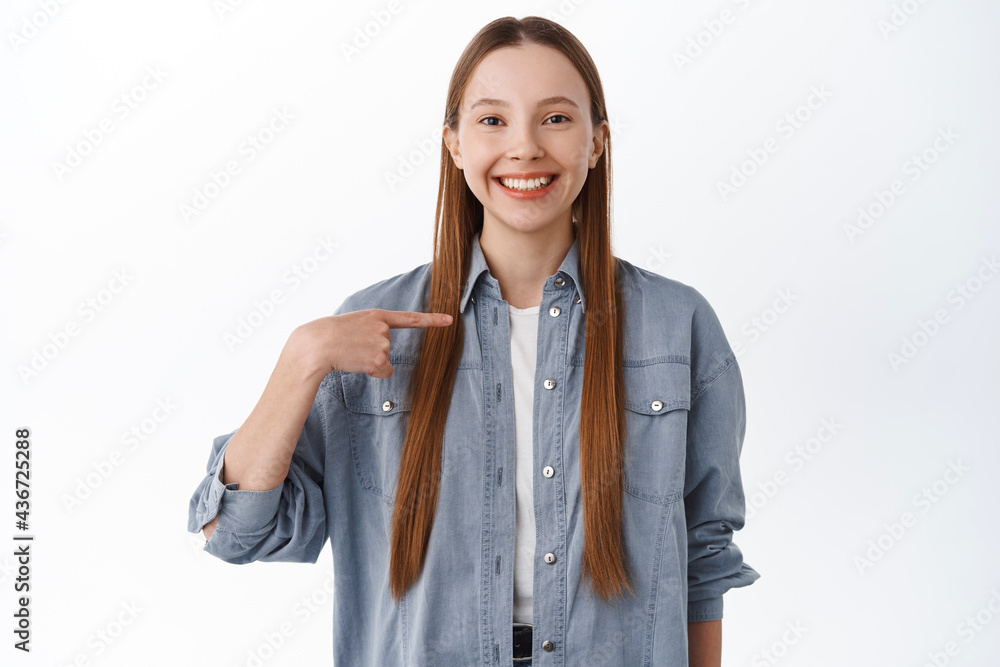 Happy confident girl pointing at herself, boasting, self-promoting, choose me gesture, volunteering to participate, standing over white background Happy confident girl pointing at herself, boasting, self-promoting, choose me gesture, volunteering to participate, standing over white background