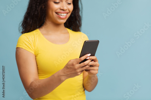 Chatting with friends. Happy black woman using smartphone texting sms message over blue background, selective focus