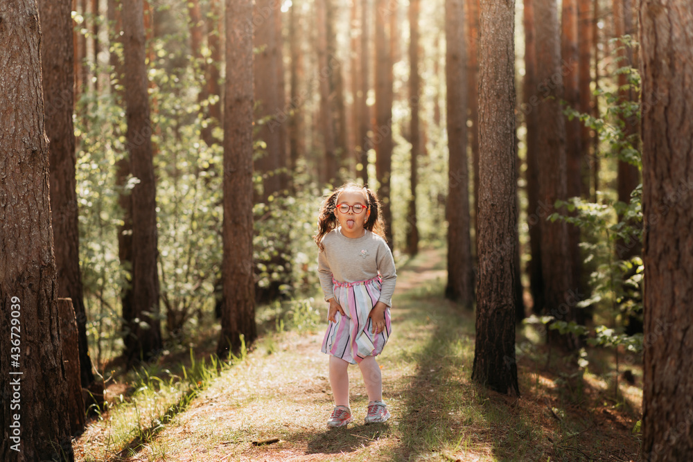 Cute girl with glasses makes a funny grimace and shows tongue in nature in summer Cute girl with glasses makes a funny grimace and shows tongue in nature in summer