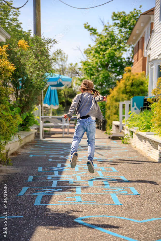 Girl jumping on a hopscotch pattern on a sidewalk in summer
